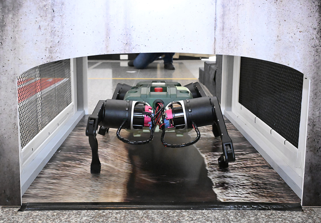 The smaller quadruped robot crawls through a narrow underground utility tunnel model designed to test its mobility in confined spaces.